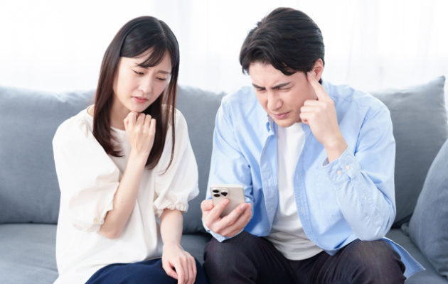 詐欺じゃないか、男女が携帯の画面をみて悩んでいる様子の写真